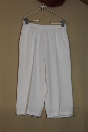 White pants hanging on a hanger against a plain wall