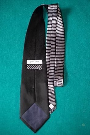 Black necktie with a blue geometric pattern and silver diagonal lines on a teal background