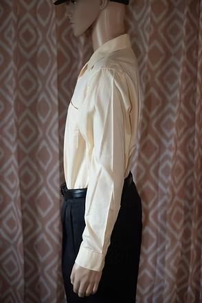 Mannequin wearing a cream button-up shirt, black pants, and a black hat against a patterned curtain backdrop