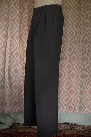 Black wide-leg pants hanging against a patterned wall.