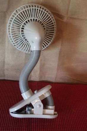 White clip-on desk fan with a flexible neck against a brown wall and red surface.