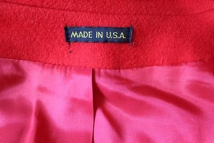Red knee-length coat with black buttons on a mannequin against a patterned curtain backdrop