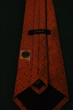 Orange necktie with a small black diamond pattern on a dark background