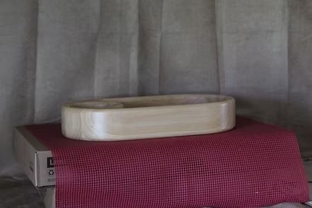 Wooden serving tray with a round bowl inset, resting on a pink textured surface against gray curtains