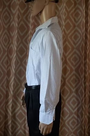Mannequin wearing a white checkered shirt and black pants against a patterned curtain backdrop