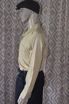 Mannequin wearing a tan shirt, black pants, and black cap against a patterned curtain backdrop