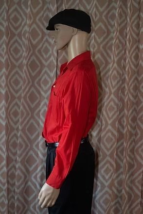 Mannequin wearing a red shirt, black pants, and black cap against a patterned curtain background