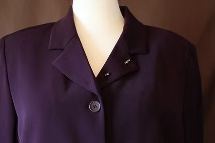 Purple women's pantsuit displayed on a mannequin against a wooden backdrop.