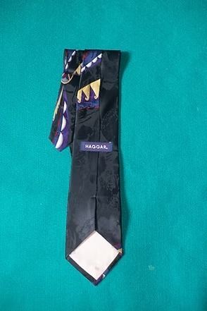 Black patterned necktie with purple and gold accents hanging on a teal background