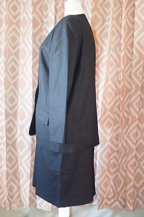 Black blazer with gold button over a black skirt on a hanger against a patterned background