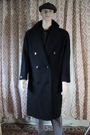 Mannequin in a black overcoat and beret standing before patterned curtains.