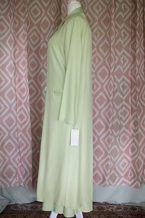 Light green long coat with matching dress displayed on a mannequin against a patterned curtain.