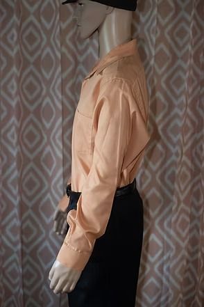Side-view mannequin in a peach button-up shirt and black pants against patterned curtains