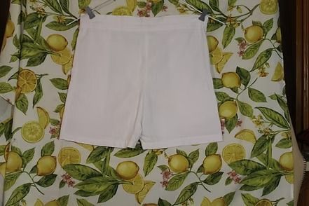 White shorts laid flat on a patterned green-and-yellow leaf-print surface