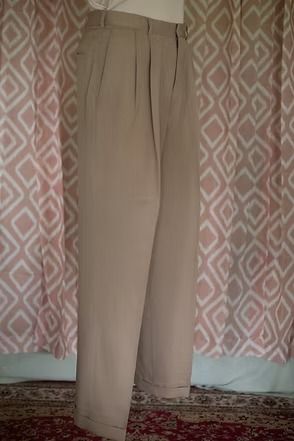 Beige pants hanging against a patterned wall, with shoes visible at the bottom.