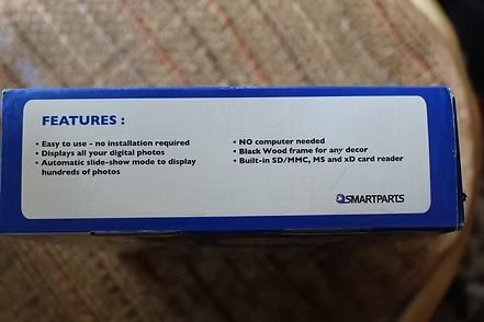 Blue digital picture frame retail box on a woven surface, showing a black frame with two people inside.