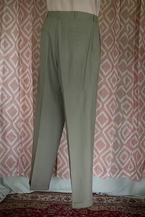 Light olive green trousers hanging in front of a patterned curtain and rug.