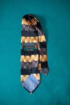 Patterned necktie with dark navy, gold, and beige geometric stripes on a teal background