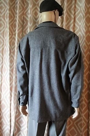 Mannequin wearing a gray jacket, black shirt, and cap in front of patterned curtains
