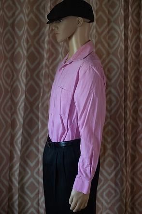 Side-view mannequin wearing a pink shirt, black cap, and black pants against a patterned curtain.