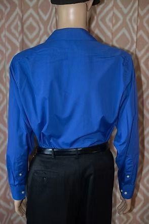 Mannequin wearing a bright blue long-sleeve dress shirt and black trousers against a patterned curtain background