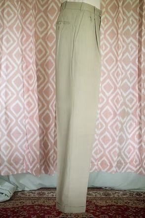 Beige pants hanging upright against a pink patterned curtain backdrop.