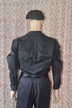 Mannequin wearing a black shirt, dark pants, and black beret against a patterned curtain backdrop