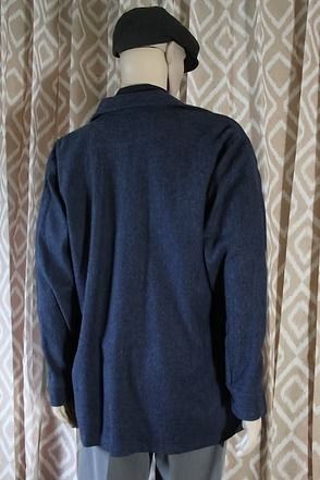 Mannequin wearing a dark jacket, black shirt, gray trousers, and a black beret against a patterned curtain.