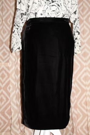 Black skirt with white floral long-sleeve top hanging against patterned wallpaper.