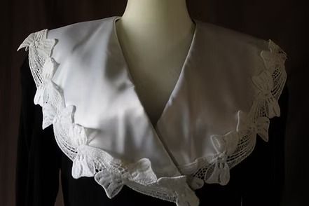 Black vintage dress with white lace collar and cuffs on a mannequin against a dark backdrop