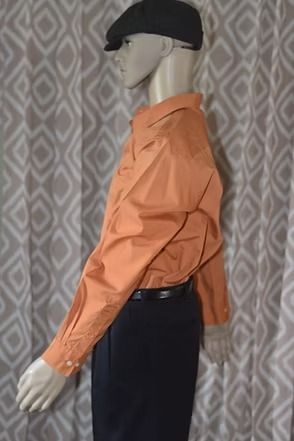 Mannequin wearing an orange shirt, dark pants, and black cap against a patterned backdrop.