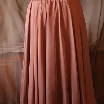 Pink pleated skirt hanging against a draped fabric background