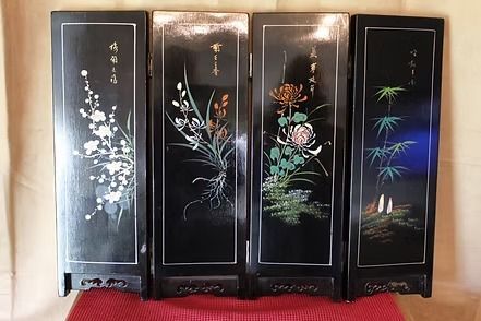 Four-panel black lacquer folding screen with floral paintings in white, blue, pink, and green on a red mat.