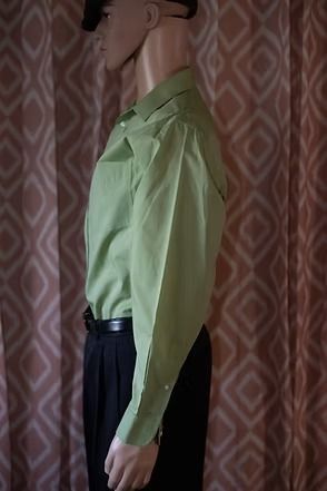 Mannequin wearing a light green button-up shirt and dark pants in side profile against a patterned curtain.