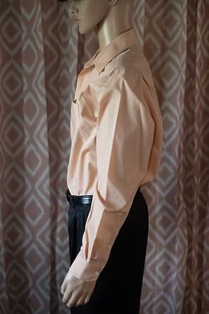 Mannequin wearing a peach button-up shirt, black pants, and a black hat against a patterned backdrop