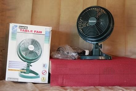 Black Holmes desk fan on a red surface against a tan background