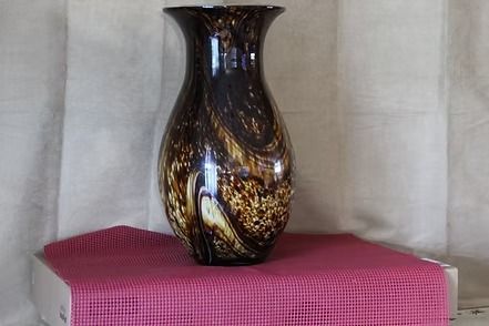 Decorative brown swirled vase on a pink textured cloth against a beige backdrop