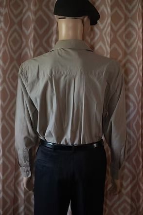 Mannequin wearing a beige button-up shirt, dark pants, and a black cap in front of patterned curtains