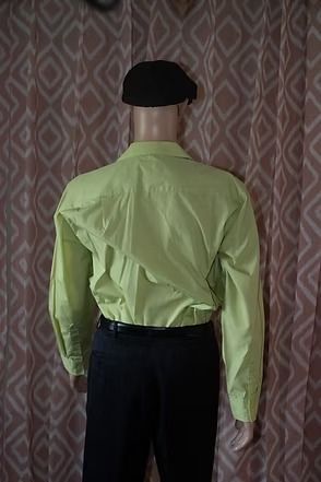 Mannequin wearing a lime green shirt, black pants, and black hat against patterned curtains