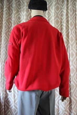 Mannequin wearing a red quarter-zip pullover, gray pants, and black cap in front of patterned curtains