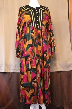 Colorful geometric-patterned long dress with black yoke and gold trim on a mannequin, against a curtain backdrop