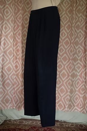 Black trousers hanging against a patterned curtain backdrop.