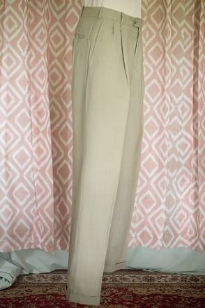 Beige pants hanging upright against a pink patterned curtain backdrop.