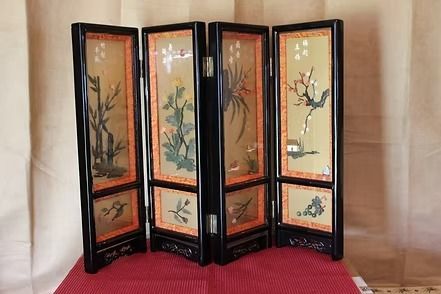 Four-panel black lacquer folding screen with floral paintings in white, blue, pink, and green on a red mat.