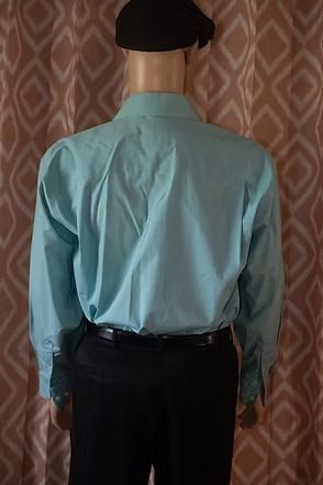 Mannequin wearing a teal button-down shirt, black pants, and black cap against a patterned curtain background