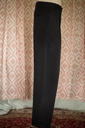 Black dress pants hanging upright in front of patterned curtains.