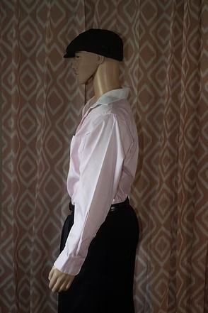 Mannequin wearing a pale pink dress shirt, dark trousers, and a black cap against patterned wallpaper