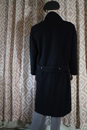 Mannequin in a black overcoat and beret standing before patterned curtains.