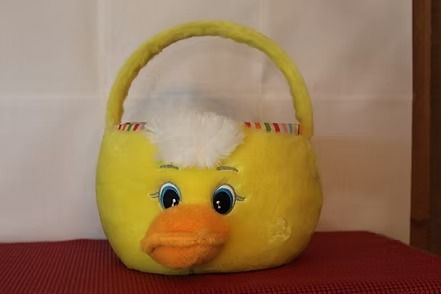 Yellow plush basket with a handle and duck face, with white stuffing on top, sitting on a red surface.