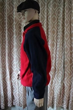 Mannequin wearing a red and navy pullover with gray pants in front of patterned curtains